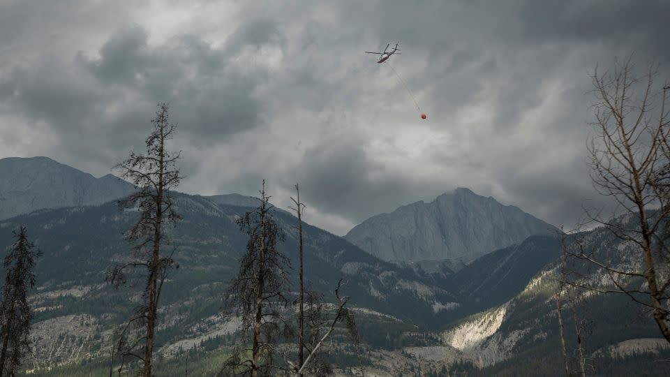 A helicopter buckets water onto smouldering fires outside of Jasper, Alberta, Canada, on July 26, 2024. Wildfires encroaching into the townsite of Jasper forced an evacuation of the national park. - Amber Bracken/The Canadian Press/AP