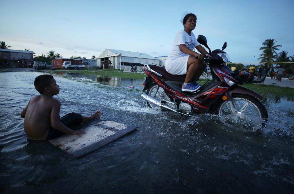 A woman rides her scooter through floodwaters occurring around high tide in a low lying area near the airport on November 27, 2019 in Funafuti, Tuvalu.