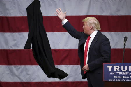 Donald Trump tosses off his overcoat as he speaks at a campaign event in an airplane hangar in Rome, New York. REUTERS/Carlo Allegri