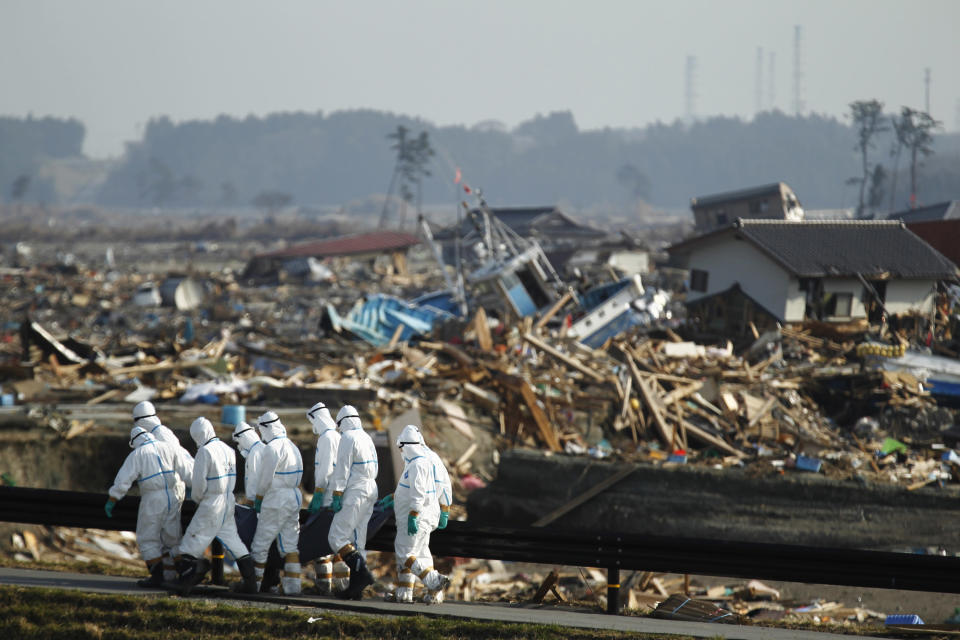 Japanese police officers carry a body during search and recovery operation for missing victims in the area devastated by the March 11 earthquake and tsunami in Namie, Fukushima Prefecture, northeastern Japan, Friday, April 15, 2011. In the background is part of the Fukushima Dai-ichi nuclear complex.