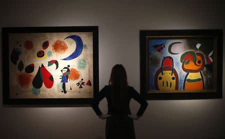 An employee at Christie's poses with Joan Miro's "L'Oiseau au plumage deploye vole vers l'arbre argente" (R) and "Painting (Women, Moon, Birds)" in London, January 8, 2015. REUTERS/Andrew Winning