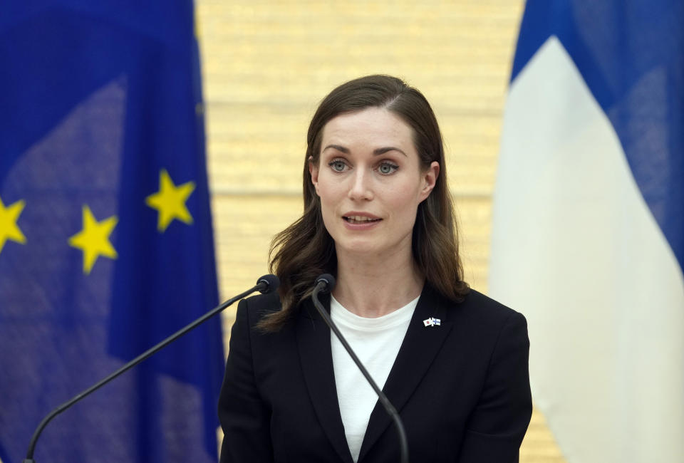 Finnish Prime Minister Sanna Marin speaks into two microphones in front of two flags.