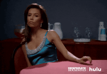 Eva Longoria in "Desperate Housewives" tapping her fingers on the table with an upset look on her face