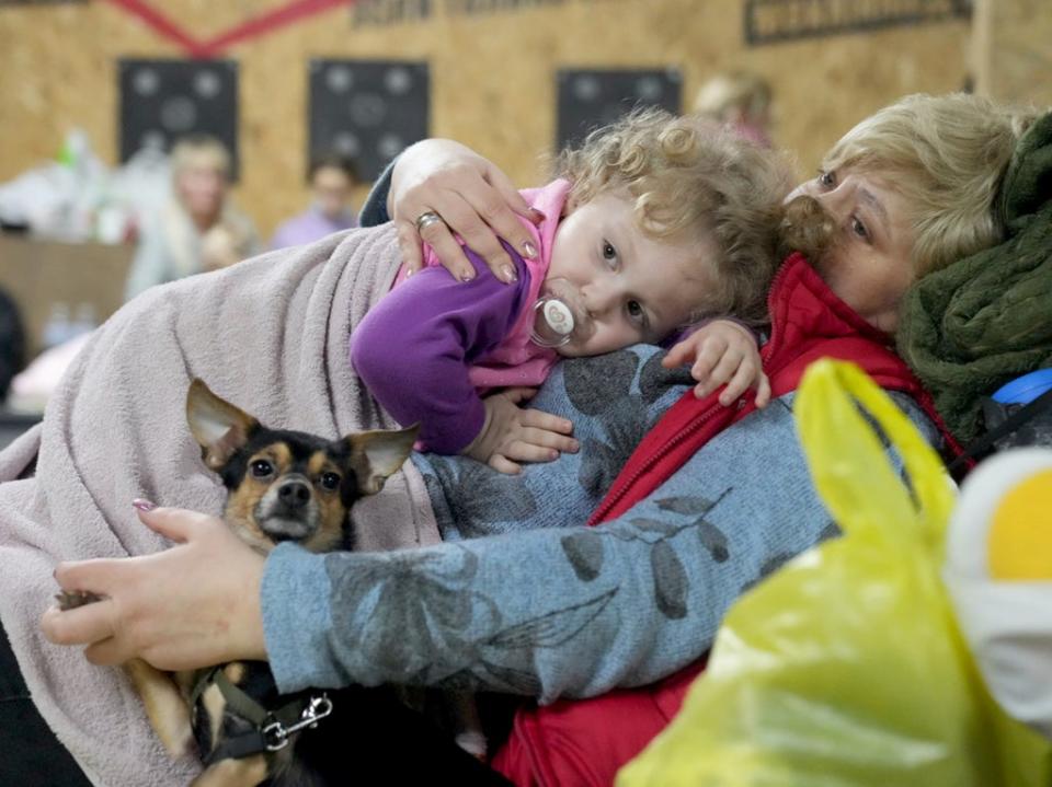 A woman holds a child and a dog in a shelter inside a building in Mariupol, Ukraine, Sunday 27 February 2022 (Evgeniy Maloletka/AP)