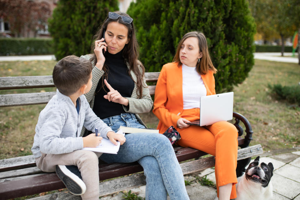 A woman on her phone with her finger raised at her child