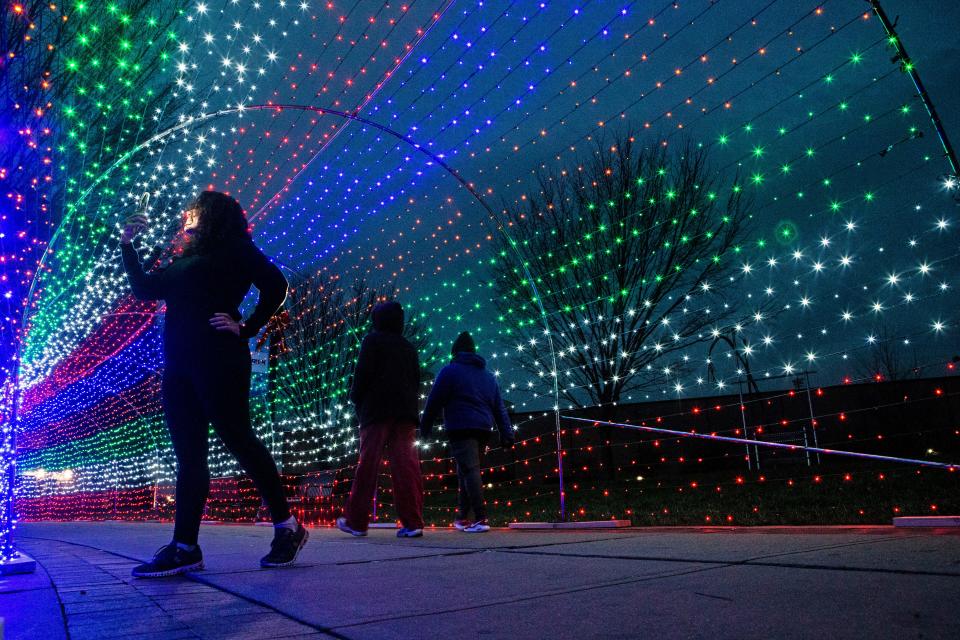 Pedestrians takes selfies and take a walk under a holiday lights tunnel along the Riverfront in Wilmington, Thursday, Dec. 8, 2022. 