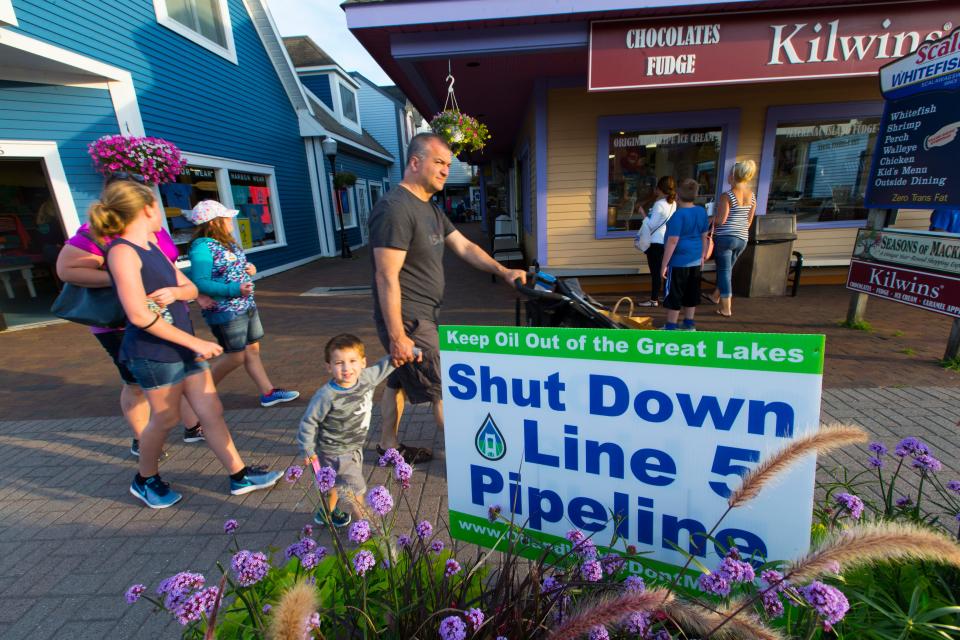 Tourists stroll past a sign opposing Enbridge's Line 5 under the Straits of Mackinac in July 2017 in Mackinaw City.