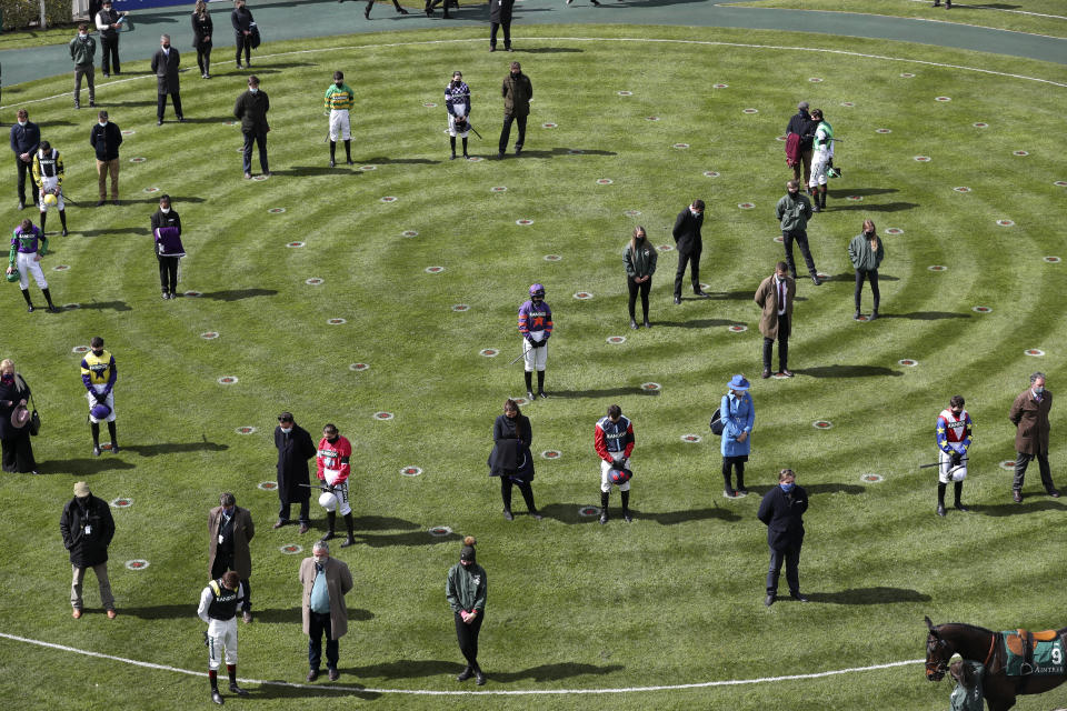 Jockey, owners and trainers stand in the parade ring during the two minute silence before the first race on the third day of the Grand National Horse Racing meeting at Aintree racecourse, near Liverpool, England, Saturday April 10, 2021. (AP Photo/Scott Heppell, Pool)