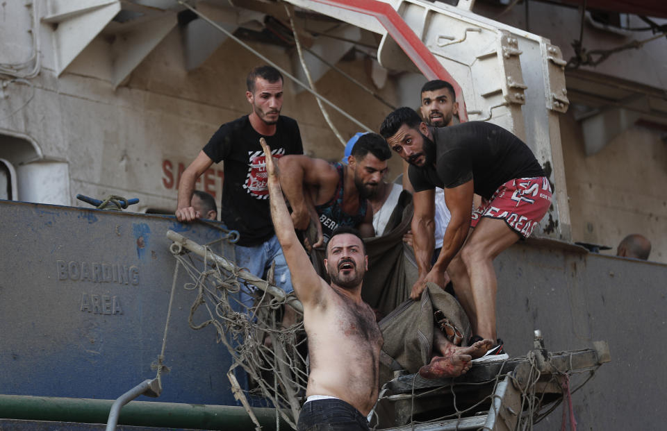 Civilians help to evacuate an injured sailor from a ship which dock near the explosion scene that hit the seaport of Beirut, Lebanon, Tuesday, Aug. 4, 2020. Massive explosions rocked downtown Beirut on Tuesday, flattening much of the port, damaging buildings and blowing out windows and doors as a giant mushroom cloud rose above the capital. (AP Photo/Hussein Malla)