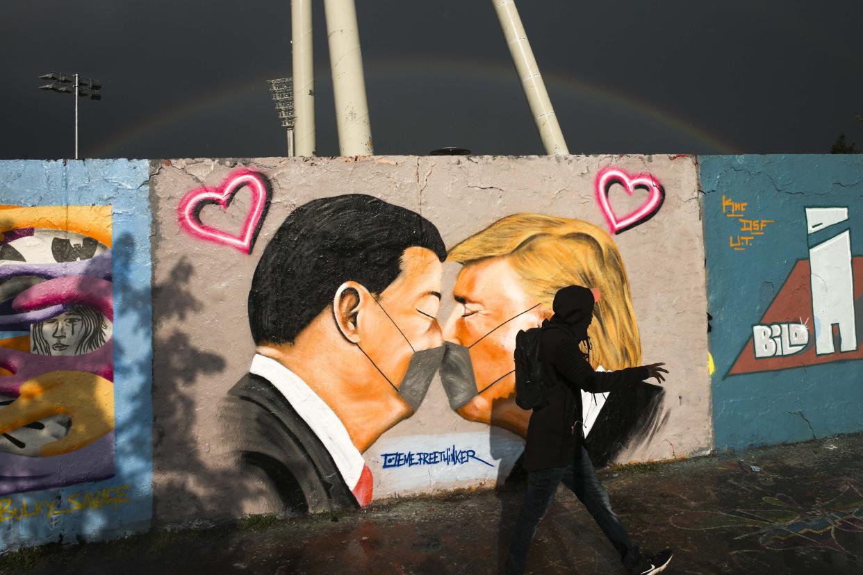 A man walks in front of graffiti depicting US President Trump, right, and China's President Xi Jinping kissing each other with face masks, displayed at a wall in the public park Mauerpark in Berlin, Germany, Wednesday, April 29, 2020. (AP Photo/Markus Schreiber)