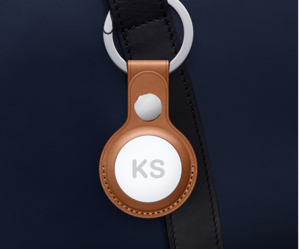 Apple Air Tag with the initials KS on the front, with a tan leather ring attaching it to a navy bag.