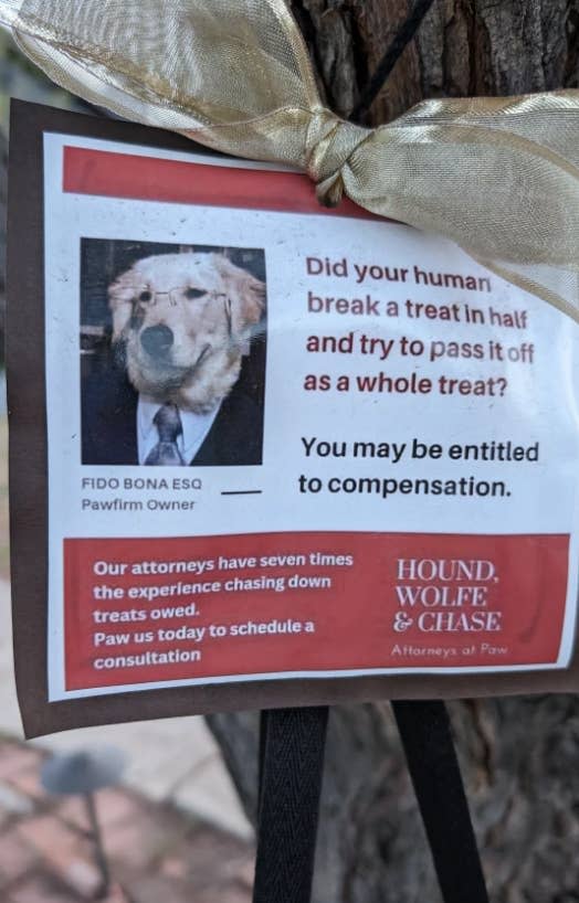Sign about dog lawyer services with humorous text and a dog's picture, attached to a tree