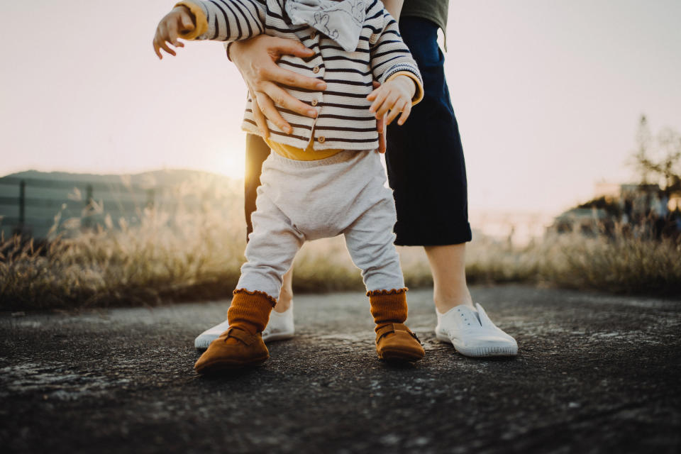 Adult helping a toddler take steps outdoors