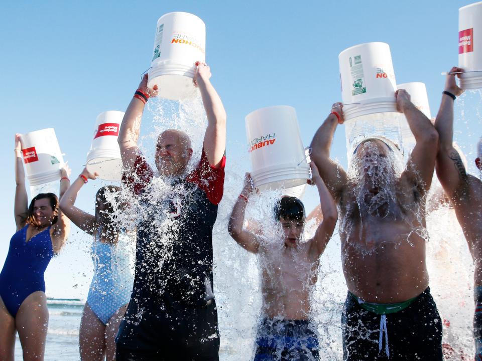 A group of people stand in a line wearing swimsuits, pouring water on their heads as part of the Ice Bucket Challenge.