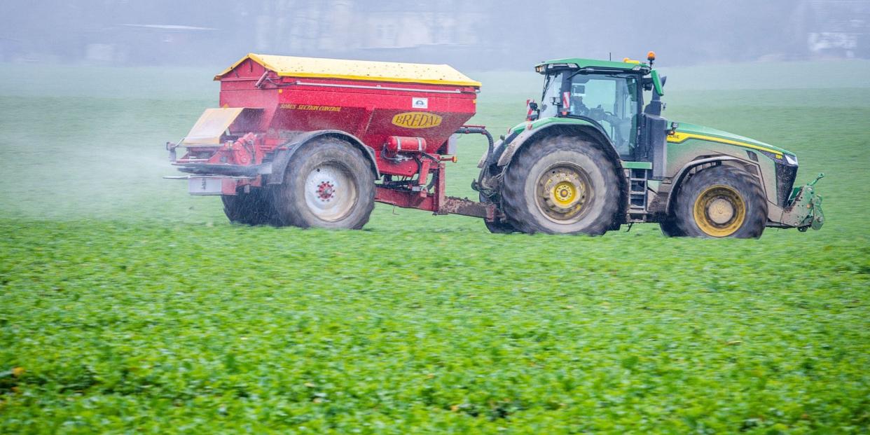 Ein Traktor fährt mit einem Streuwagen über ein Feld und bringt Dünger aus.<span class="copyright">dpa</span>