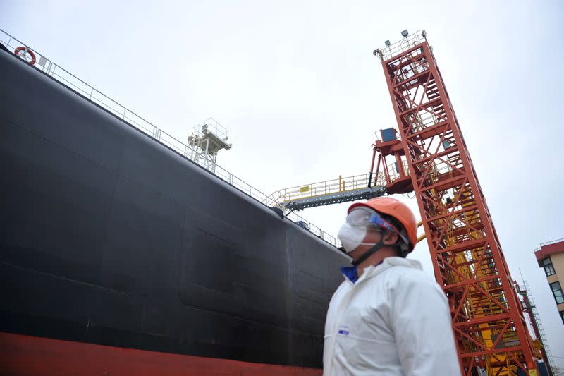 Dock worker wearing a face mask looks at an oil tanker unloading crude oil at a port in Qingdao