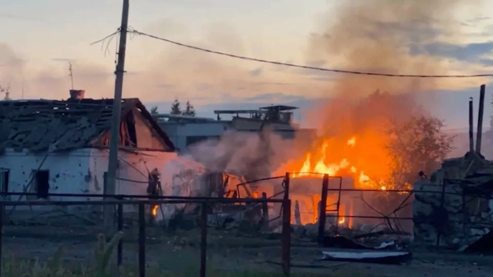 A damaged white one-story building and a fire are seen in a still from a video