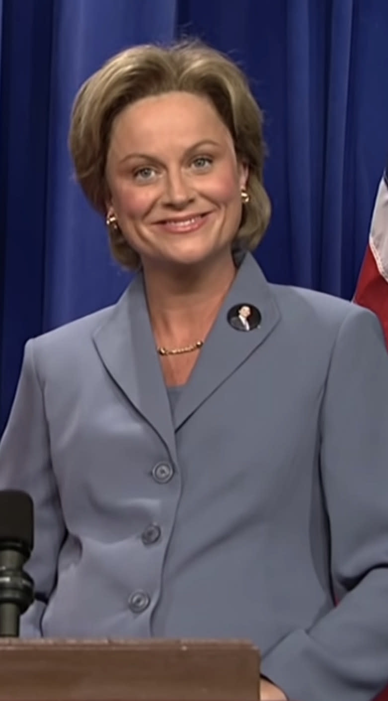 Poehler wearing a blue pantsuit and short hairdo like Hillary Clinton