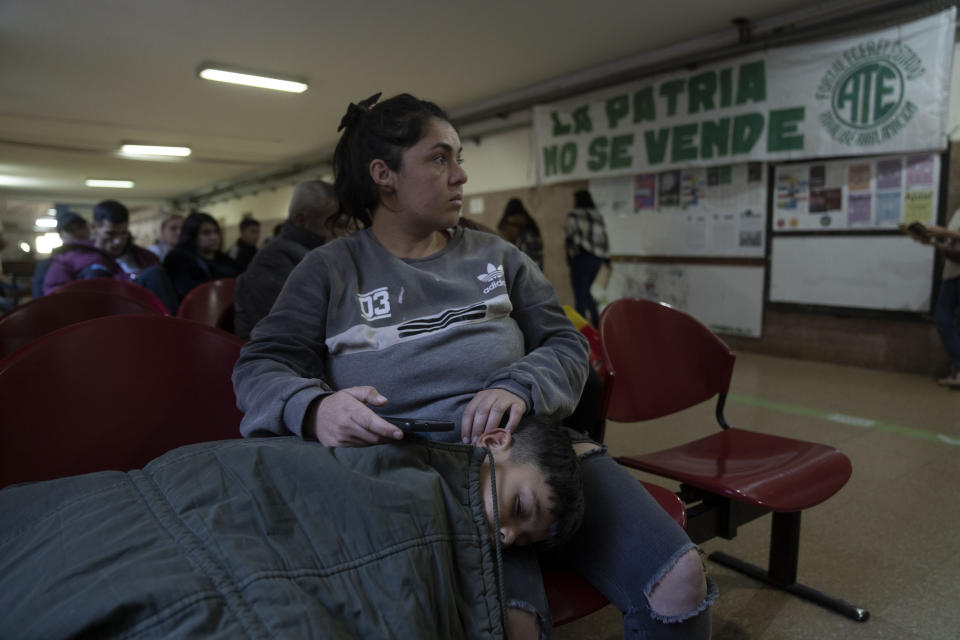 Yésica García y su hijo Juan Paz esperan a ser atendido en la sala de emergencias del Hospital de Clínicas, donde hay un cartel sindicalista de protesta en Buenos Aires, Argentina, el jueves 18 de abril de 2024. Personal médico y estudiantes protestan fuera del hospital, que depende financieramente de la Universidad de Buenos Aires (UBA), contra el congelamiento presupuestario de la UBA dispuesto por el presidente argentino, Javier Milei, como parta de sus medidas de austeridad. (AP Foto/Víctor R. Caivano)