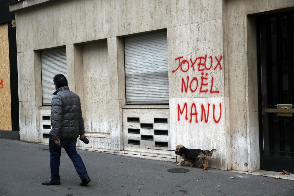 A man walks his dog past a tag reading : Happy Christmas Manu, referring to French President Emmanuel Macron