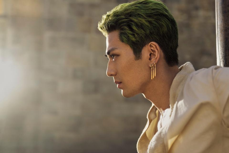 mackenyu as zoro in one piece, a young man with three gold dangling earrings, short green hair