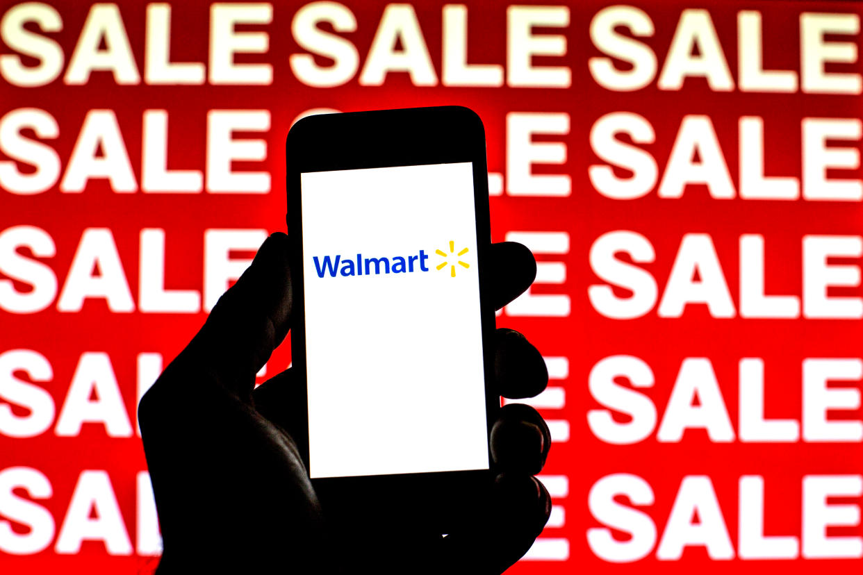 Hand holding a phone displaying a Walmart Logo against a Sale banner