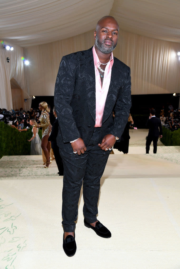 Corey Gamble wears a brightly colored button up shirt under a dark suit jacket and matching slacks