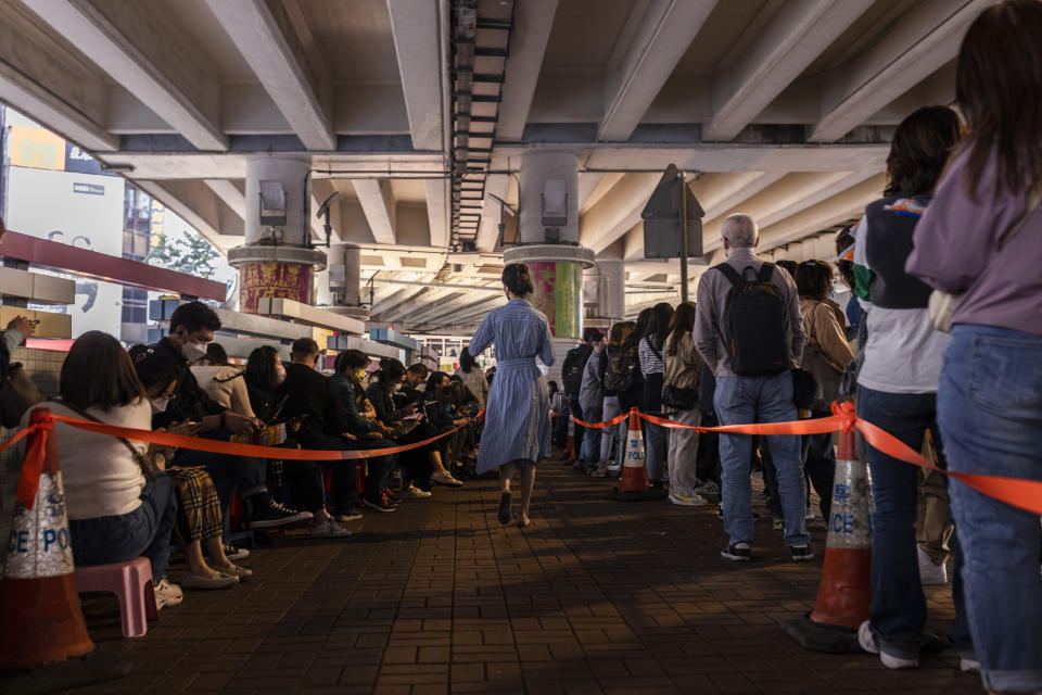 A pedestrian passes lines of customer waiting to receive a "villain hitting" ceremony on the day of "ging zat," as pronounced in Cantonese, which on the Chinese lunar calendar literally means "awakening of insects," under the Canal Road Flyover in Hong Kong on Monday, March 6, 2023. (AP Photo/Louise Delmotte)