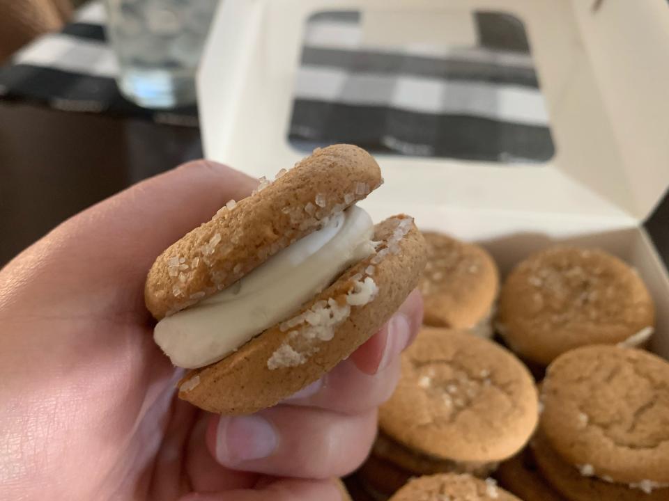 hand holding trader joes trader joe's gingerbread sandwich cookie in front of box of them