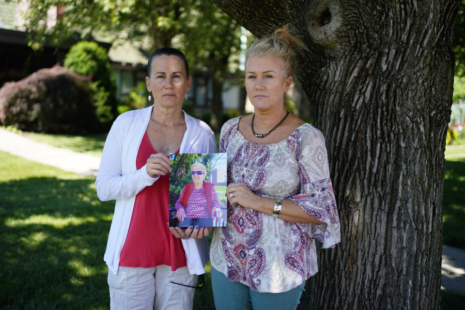 Angela Ermold, right, and her sister, Denise Gracely, pose with a photo of their mother, Marian Rauenzahn, Thursday, June 17, 2021, in Fleetwood, Pa. Pandemic restrictions are falling away almost everywhere — except inside many of America’s nursing homes. “They have protected them to death,” said Gracely. (AP Photo/Matt Slocum)