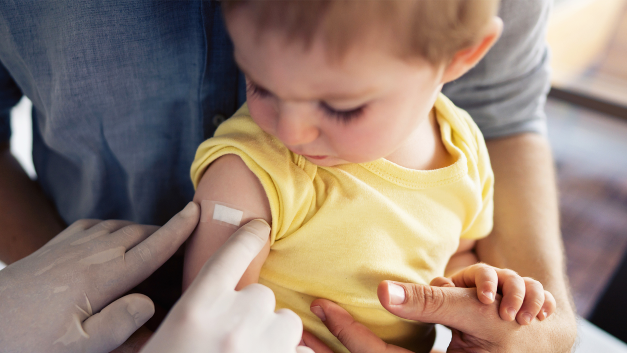 Young child looks on as bandage is applied to arm after Omicron Covid booster shot.