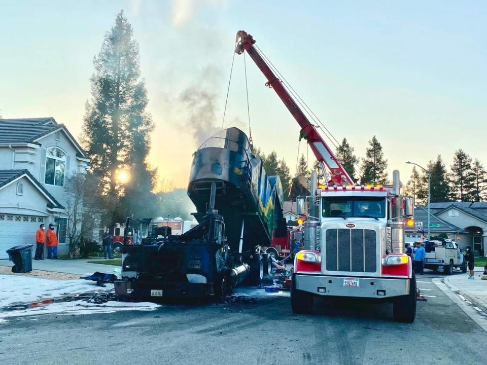 A crane lifts the back end of a garbage truck after it caught on fire in Fresno on Wednesday, Jan. 26, 2022.