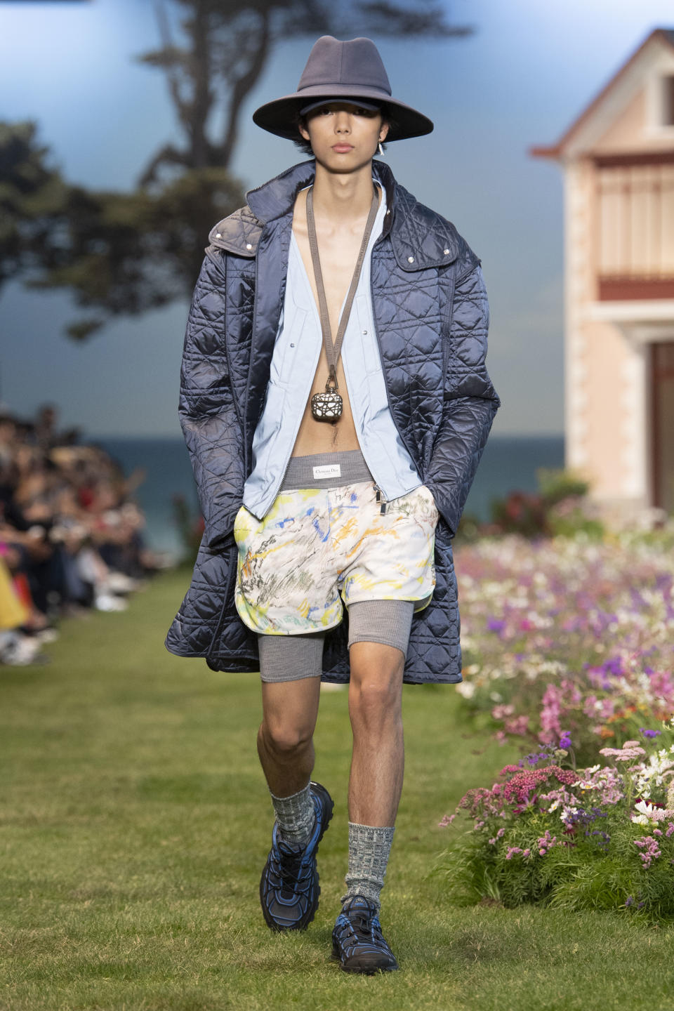 A quilted satin overcoat layered over a sportier silhouette that included boxer shorts and compression biker short, plus a double-layered hat at Dior summer ’23 men’s. - Credit: YANNIS VLAMOS