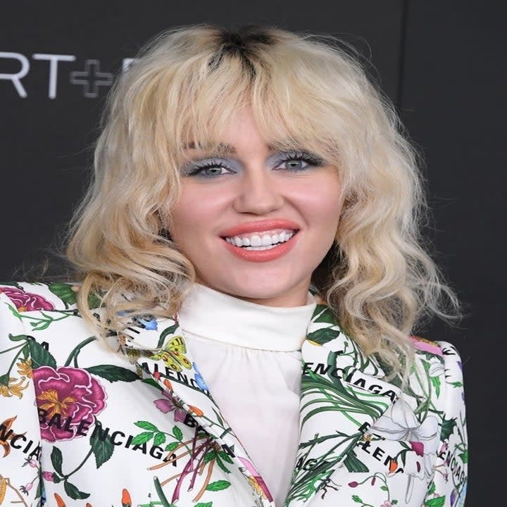 A closeup of Miley at a red carpet event wearing a floral printed jacket with Balenciaga written all over it