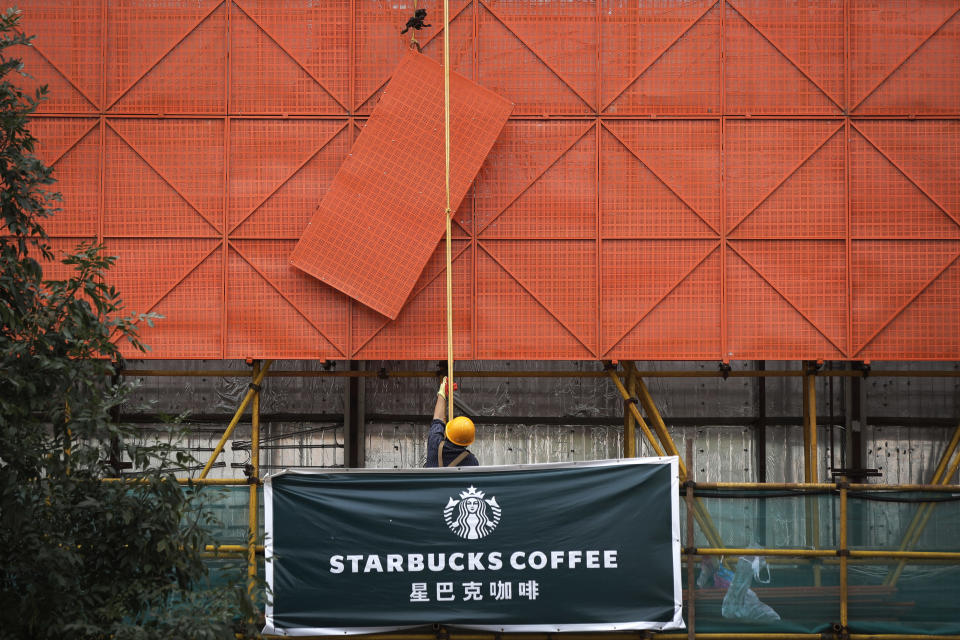 FILE - In an Aug. 14, 2018 file photo, a worker lifts a protection steel frame on a Starbucks cafe banner hanging outside a shopping mall under renovation in Beijing. A report out Monday, May 11, 2020, found that China’s direct investment in the United States dropped from $5.4 billion in 2018 to $5 billion last year, the lowest level since the recession year of 2009. (AP Photo/Andy Wong, File)