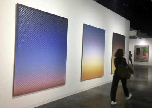 A visitor walks by three pieces by Rob Pruitt that depict a fenced US-Mexico border at different times of day