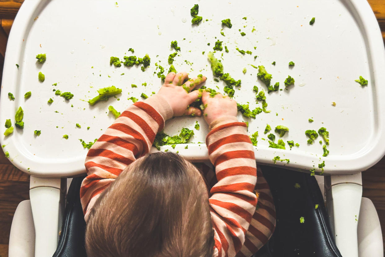 Toddler eating broccoli in high chair Getty Images/Gabriel Mello