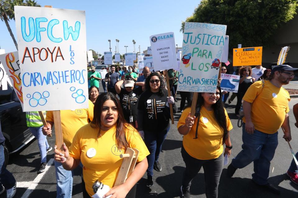 Picketers hold signs and march outside a carwash.