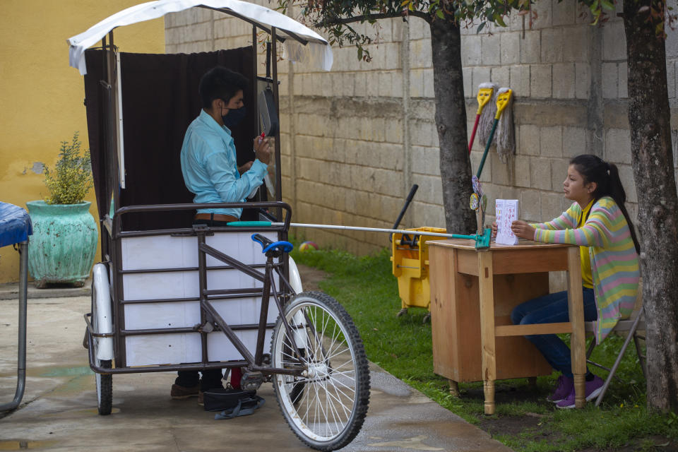 Gerardo Ixcoy teaches fractions to 14-year-old Brenda Morales, from his secondhand adult tricycle that he converted into a mobile classroom, in Santa Cruz del Quiche, Guatemala, Wednesday, July 15, 2020. The 27-year-old teacher deploys a sponge mop to serve as a safe distance reminder between him and his students, amid the new coronavirus pandemic. (AP Photo/Moises Castillo)