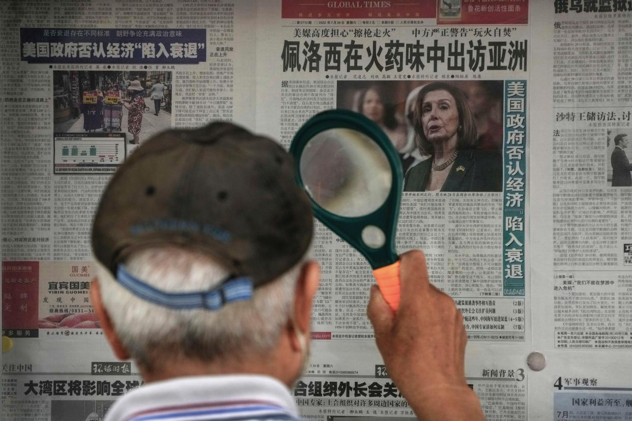 A man uses a magnifying glass to read a newspaper headline reporting on U.S. House Speaker Nancy Pelosi's Asia visit, at a stand in Beijing, Sunday, July 31, 2022. Pelosi confirmed Sunday she will visit four Asian countries this week but made no mention of a possible stop in Taiwan that has fueled tension with Beijing, which claims the island democracy as its own territory. (AP Photo/Andy Wong)