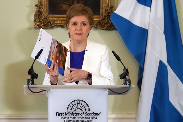 Nicola Sturgeon holding a document in front of a Scotland flag