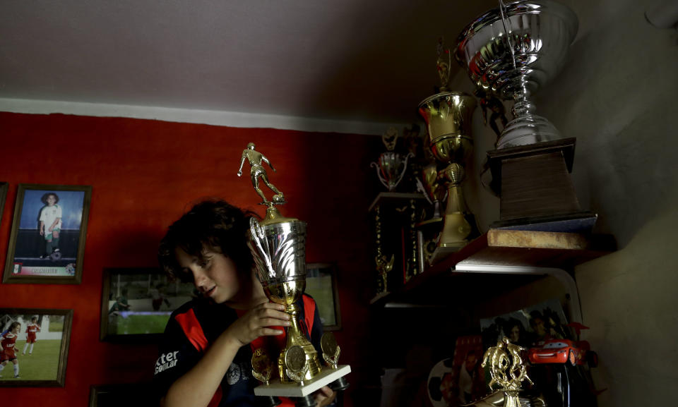 En esta foto del 19 de noviembre de 2016, Thiago “Coco” Perugini muestra uno de sus trofeos a periodistas dentro de su cuarto a las afueras de Buenos Aires, Argentina. Thiago recientemente fue transferido a la división juvenil de San Lorenzo y sus padres pintaron su pared como las del club, en rojo y azul. (AP Foto/Natacha Pisarenko)