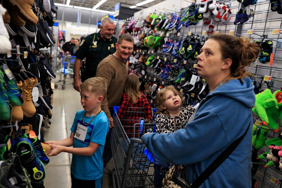 Jill Burden, right, looks on to select shoes with daughter, Skyler, 2, in the cart, Dawson, 8, left, selecting, and husband Darryl, talking with daughter Frankie, 5, as Sgt. Wayne Herrington, back, helps and Thursday, Dec. 7, 2023 at Walmart Supercenter in Yulee, Fla. A total of 150 local children from Bryceville Elementary, Callahan Intermediate and Callahan Elementary took part in the annual Nassau County Sheriffs Office (NCSO) “Shop with Cops” program. The event pairs children in need with local law enforcement to purchase holiday gifts. Each child is free to spend $75 on clothing and school supplies, and $75 on toys. The funds were raised through the NCSO Charities Inc. The hope is to give the youth a pleasant holiday while creating a positive relationship with law enforcement. [Corey Perrine/Florida Times-Union]