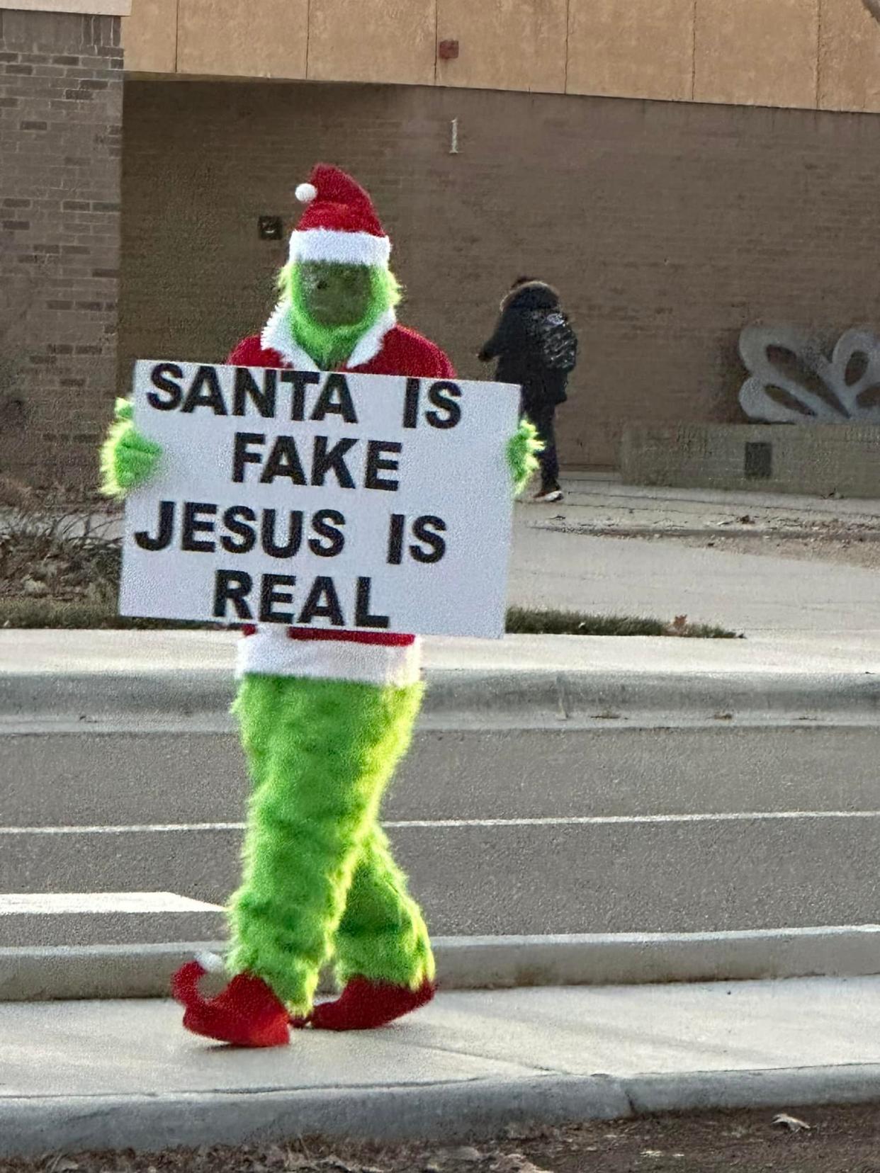 David Grisham, dressed as the Grinch, stands outside of Sleepy Hollow Elementary School with a sign telling children "SANTA IS FAKE" on Monday in Amarillo.