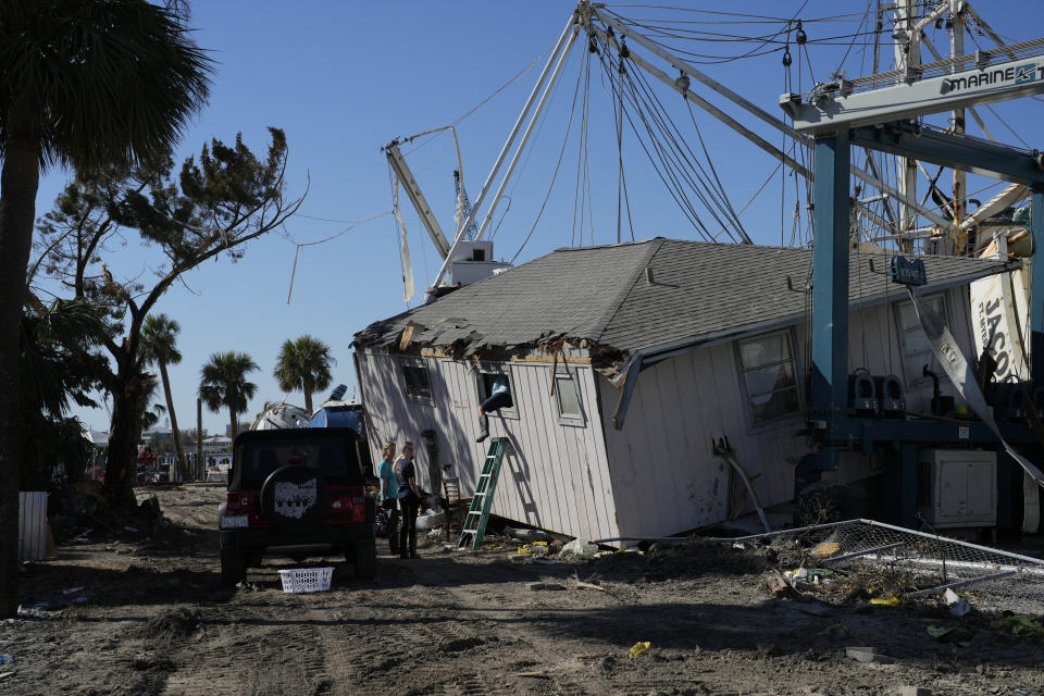 Lorie Longi, 54, left, looks on as her boyfriend climbs through the window of what was her second story apartment, as they try to salvage water-soaked belongings from inside following the passage of Hurricane Ian, on San Carlos Island in Fort Myers Beach, Fla., Friday, Oct. 7, 2022. (AP Photo/Rebecca Blackwell)