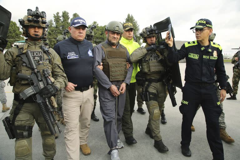 En esta foto publicada por la Oficina de Prensa de la Presidencia de Colombia aparece la escolta policial de Dairo Antonio Úsuga, centro, también conocido como "Otoniel", líder del violento cartel Clan del Golfo antes de su extradición a EEUU en un aeropuerto militar en Bogotá, Colombia, el miércoles 4 de mayo de 2022. (Oficina de Prensa de la Presidencia de Colombia via AP)