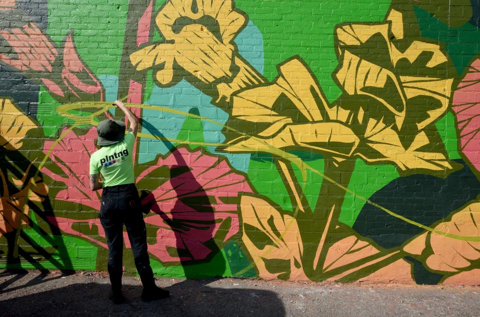 Artist George Rose of Australia works on painting a vine for the finishing touches on her abstract mural on the wall at Logan Charles Salon.   