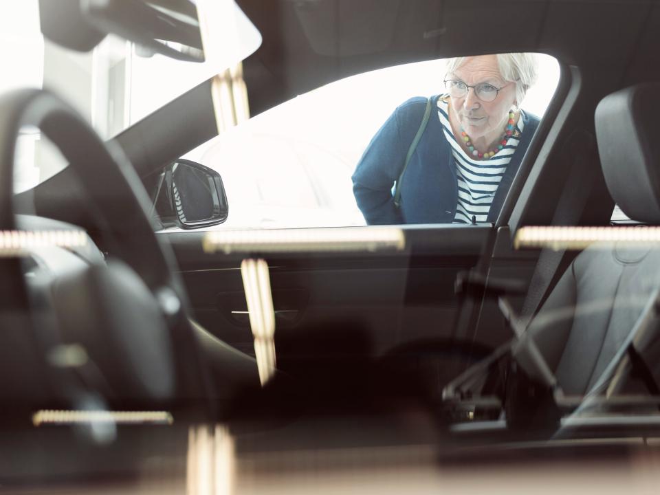an older woman looks into an empty car from the passenger side