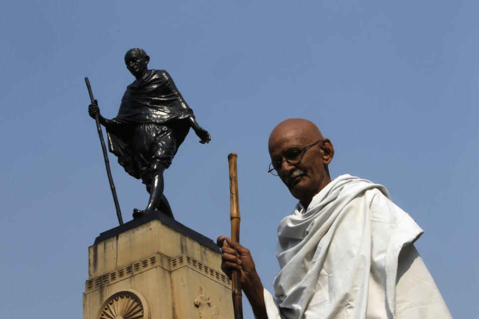 Mahesh Chaturvedi, who dresses up like Mahatma Gandhi, poses for a photo in front of a Gandhi statue in New Delhi