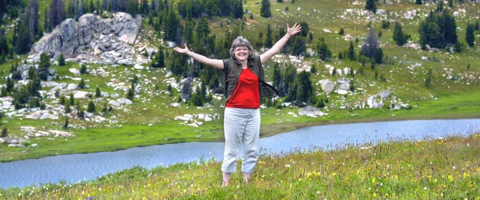 Woman spreads her arms wide to embrace the scenic beauty of Beartooth Pass in Wyoming.